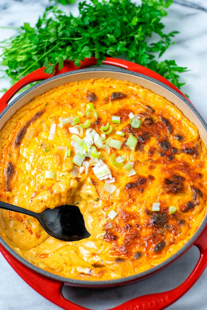 Casserole dish with the vegan Buffalo Dip with a black spoon sticking in it.