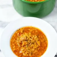 A portion of the Cabbage Roll Soup on a white soup place with the large green pot in the background.