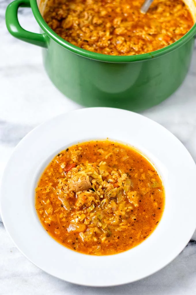 A portion of the Cabbage Roll Soup on a white soup place with the large green pot in the background.