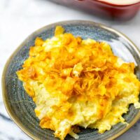 A portion of the Funeral Potatoes on a small plate with the casserole dish in the background.