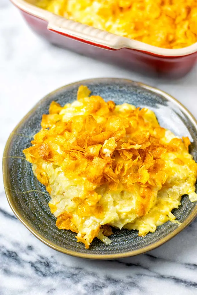 A portion of the Funeral Potatoes on a small plate with the casserole dish in the background. 