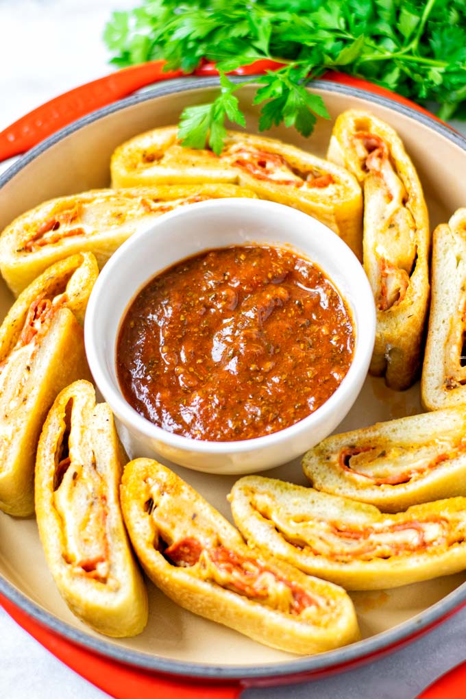 Sliced Stromboli are arranged in a round serving dish with a small bowl of tomato dipping sauce in the middle.