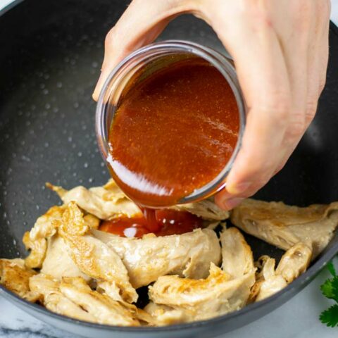 Nashville Hot Sauce is poured over vegan chicken in a frying pan.