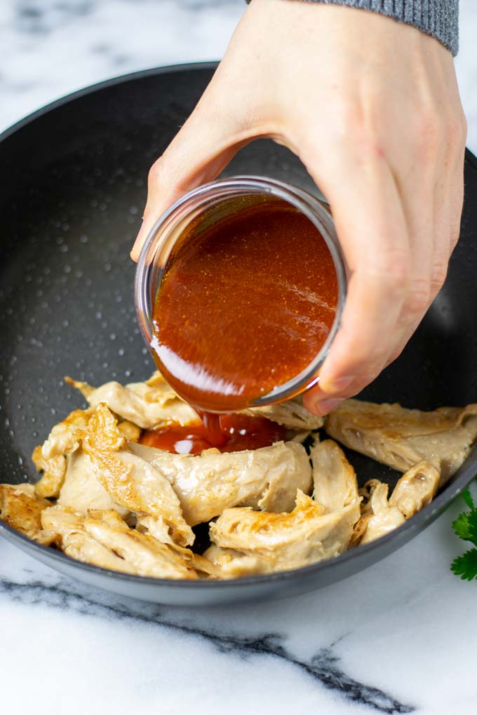 Nashville Hot Sauce is poured over vegan chicken in a frying pan.