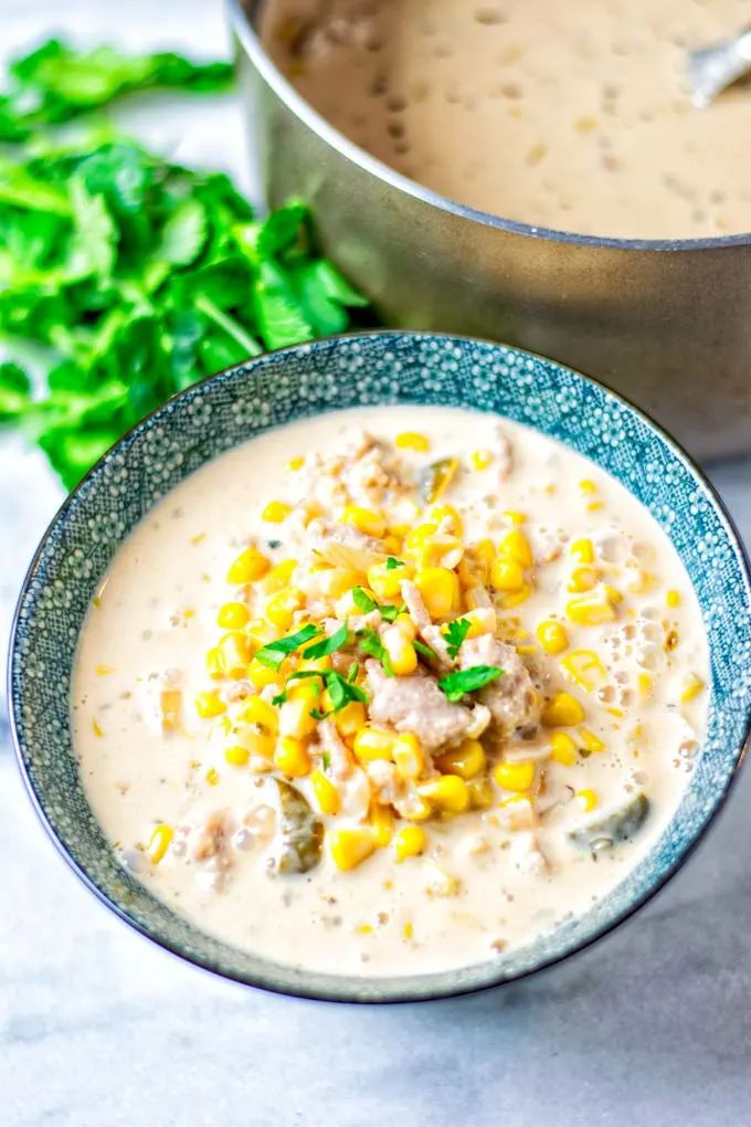 View of a portion of the Corn Soup in a bowl, decorated with fresh cilantro, and the soup pot visible in the background.