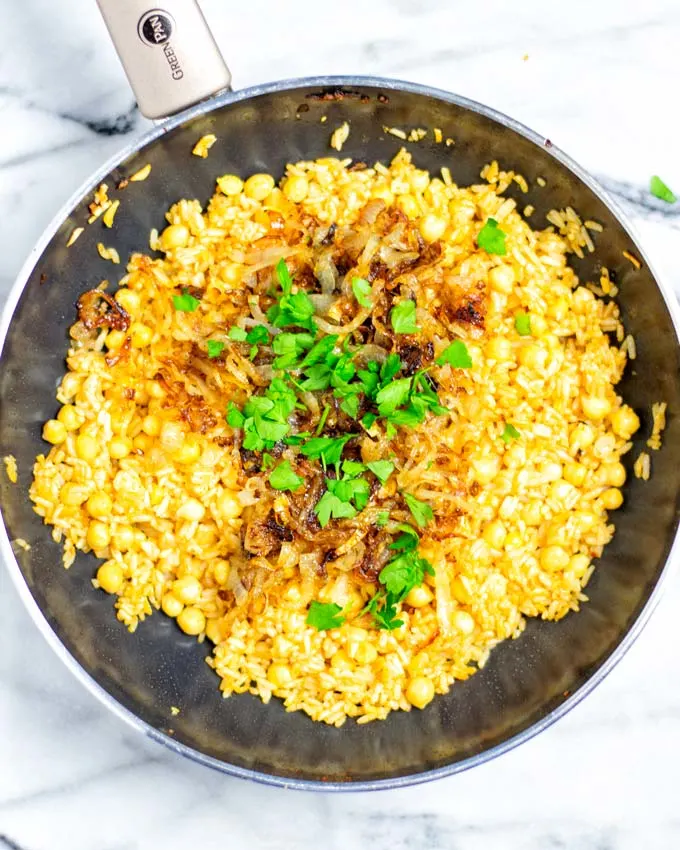 Top view of a frying pan with the Crispy Rice topped with caramelized onions and fresh herbs.