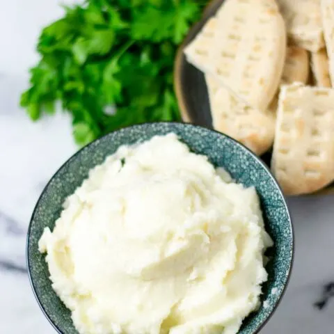 The Garlic Sauce in a serving bowl is shown with roasted pita bread and herbs in the background.