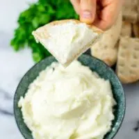 A hand is holding a slice of pita bread after it has been dipped into the garlic sauce.