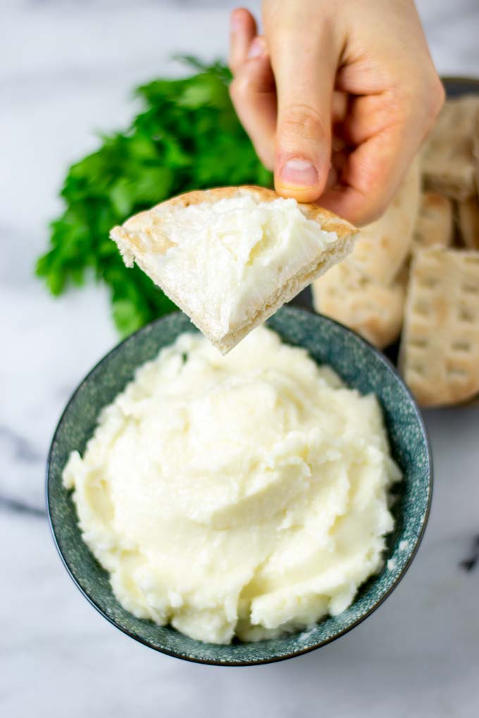 A hand is holding a slice of pita bread after it has been dipped into the garlic sauce.