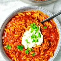 Top view of a large plate filled with a portion of the Lasagna Soup, with a dollop of the vegan cheese topping, and fresh herbs.