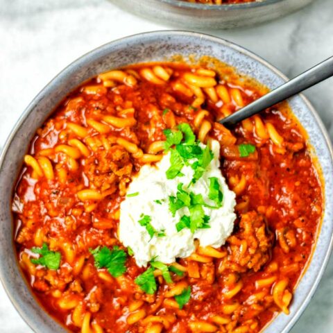 Top view of a large plate filled with a portion of the Lasagna Soup, with a dollop of the vegan cheese topping, and fresh herbs.