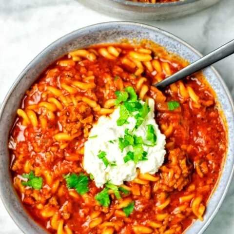 Top view of a large plate filled with a portion of the Lasagna Soup, with a dollop of the vegan cheese topping, and fresh herbs.