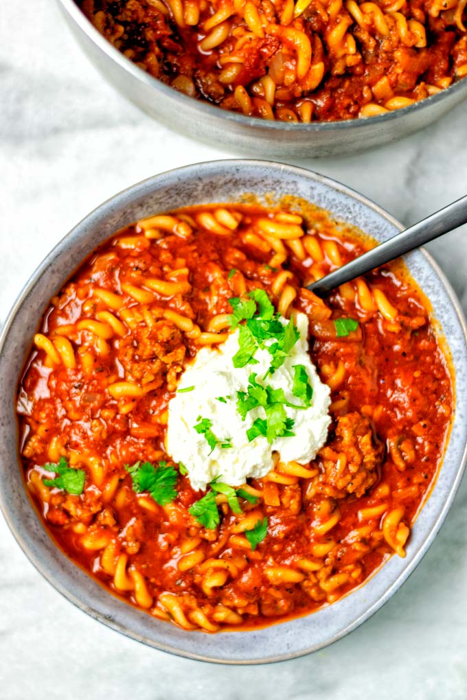 Top view of a large plate filled with a portion of the Lasagna Soup, with a dollop of the vegan cheese topping, and fresh herbs.