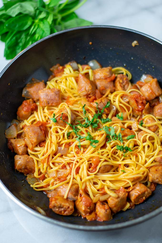 View of a pan with the Tomato Pasta, with sausage pieces clearly visible, garnished with fresh herbs.