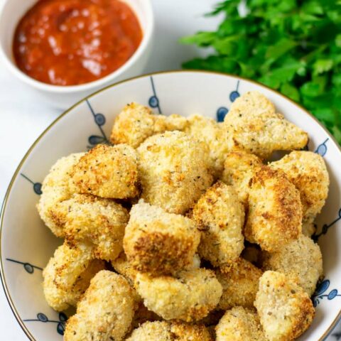 Cauliflower Bites in a large bowl with dipping sauce in the background.