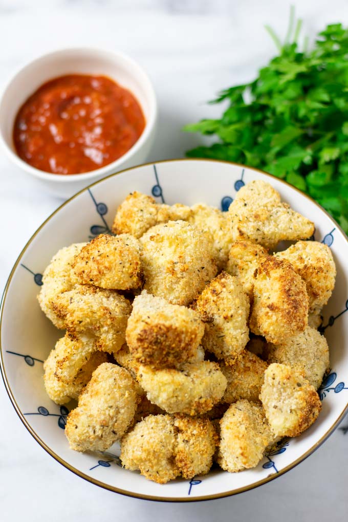 Cauliflower Bites in a large bowl with dipping sauce in the background.