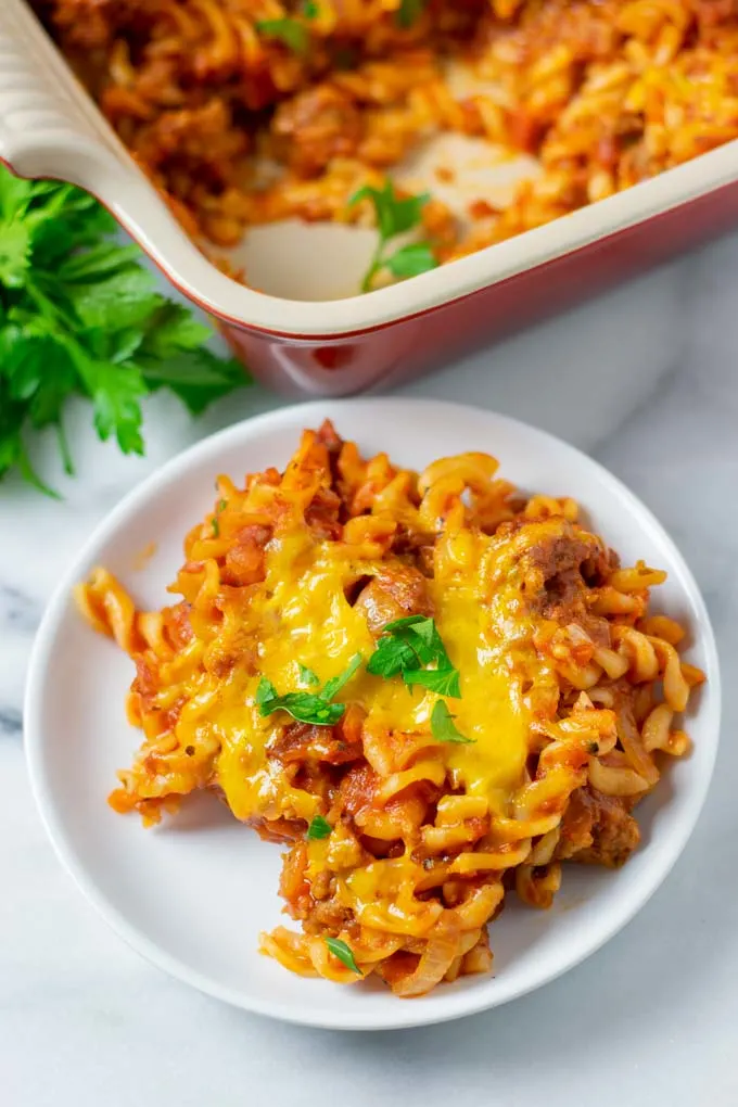 A portion of the Hamburger Casserole on a small white plate with the casserole in the background.