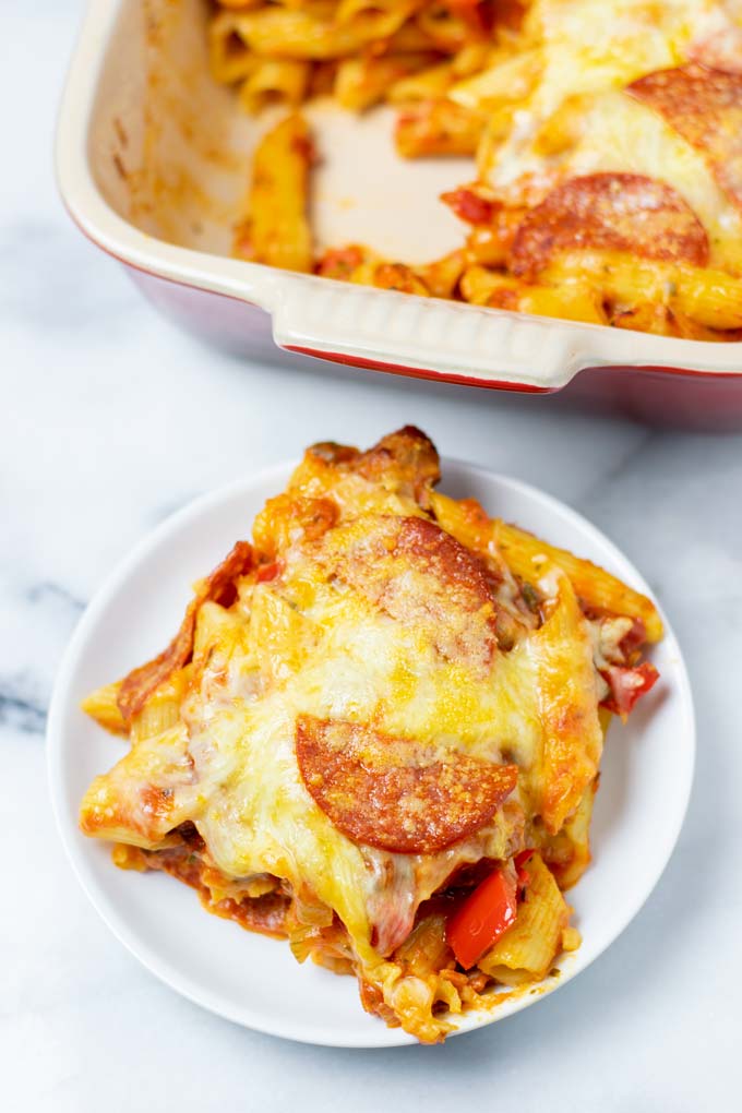 A portion of the Pizza Casserole on a small white plate with the baking dish in the background.