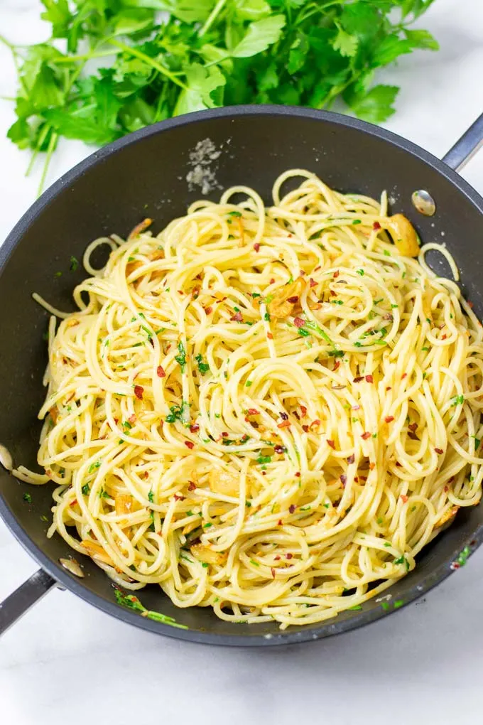 Top view of a pan with the Spaghetti aglio e olio with fresh herbs in the background.