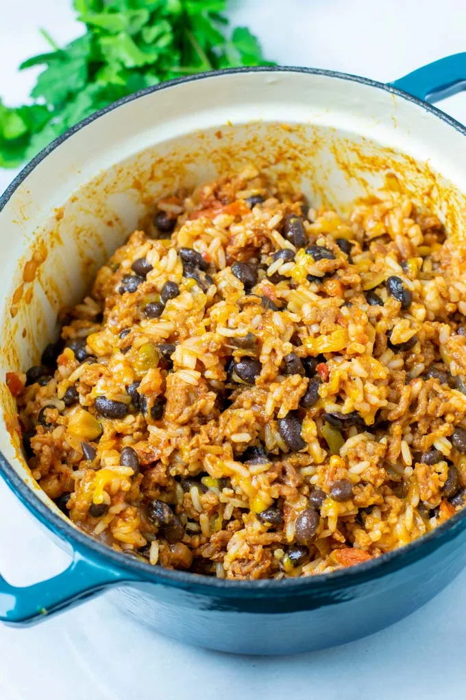 The ready Taco Rice in a large blue pot with fresh herbs in the background.