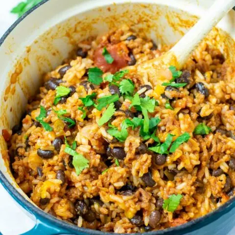 View of the Taco Rice with a wooden spoon and some fresh herbs sprinkled over it.