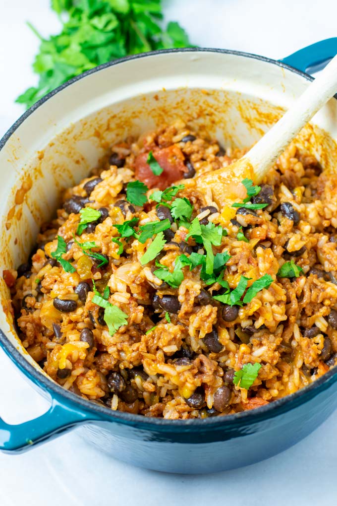 View of the Taco Rice with a wooden spoon and some fresh herbs sprinkled over it.