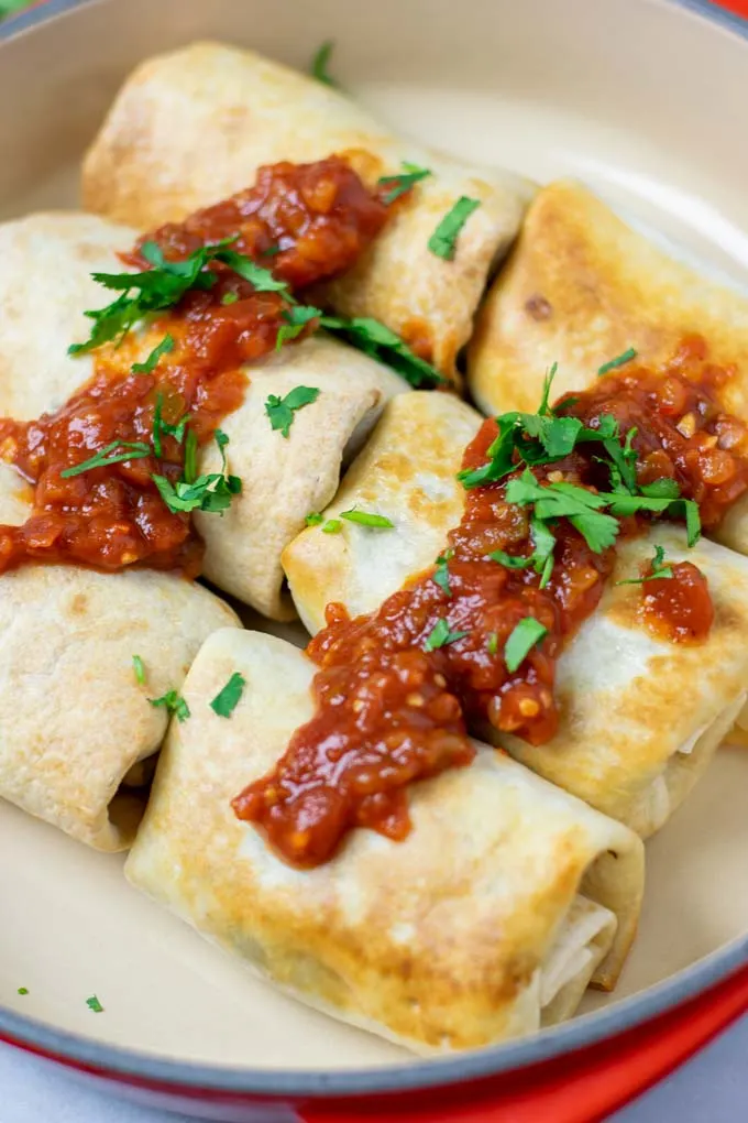 Baked and fried versions of the Chimichangas in a dish, covered with extra salsa and fresh herbs.