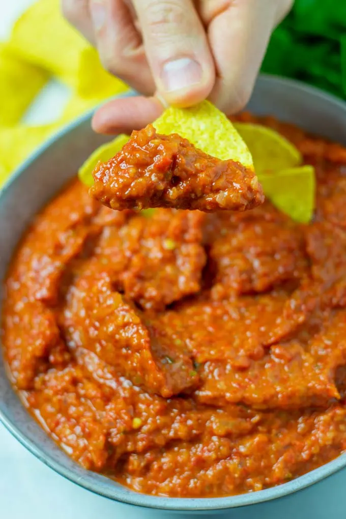 A taco chip with sauce is lifted from the bowl.