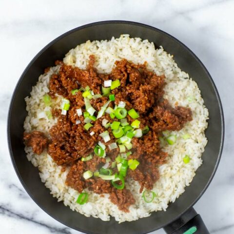 A pan with fried rice covered with vegan beef and scallions.