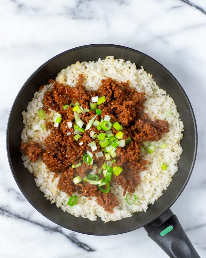 A pan with fried rice covered with vegan beef and scallions.