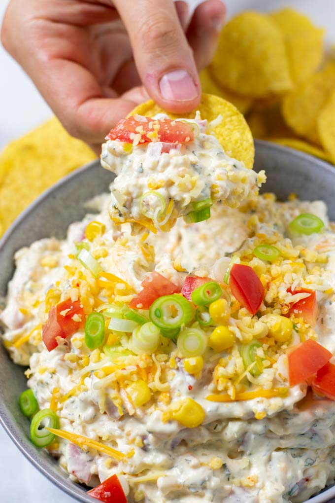 A hand is holding a nacho chip that has been dipped into the Fiesta Ranch Dip.