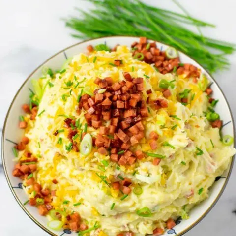 A large serving bowl of the Loaded Mashed Potatoes, topped with extra vegan bacon, cheese, and scallions.