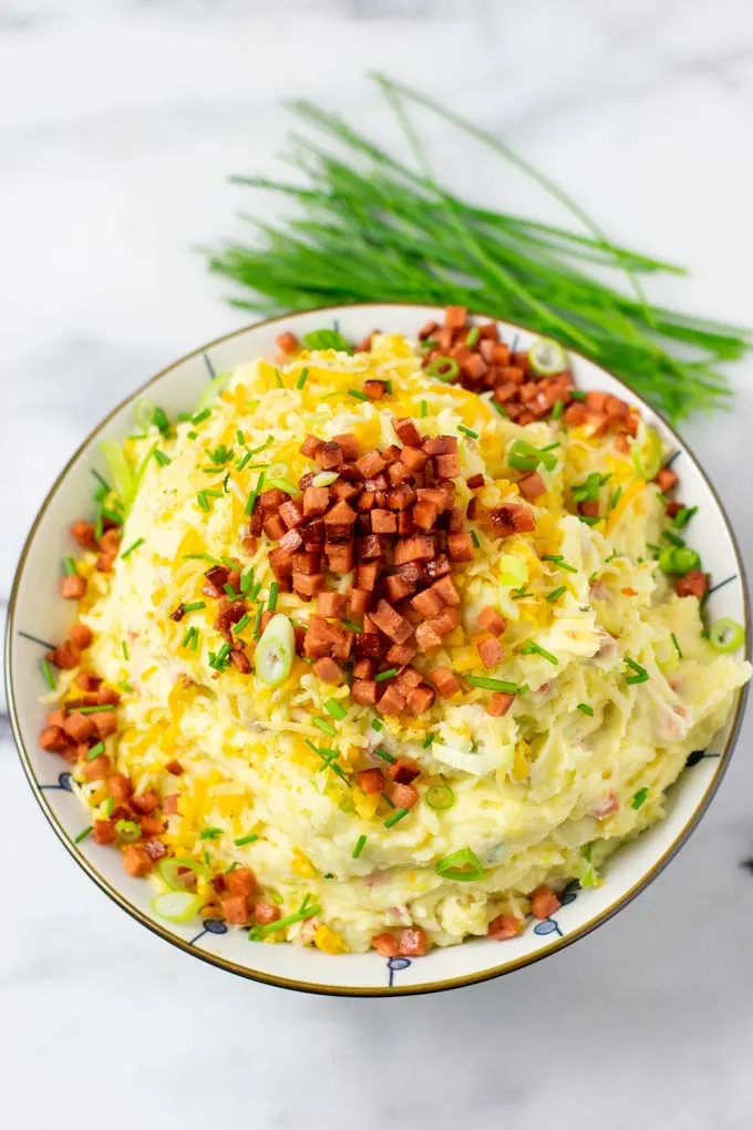 A large serving bowl of the Loaded Mashed Potatoes, topped with extra vegan bacon, cheese, and scallions.