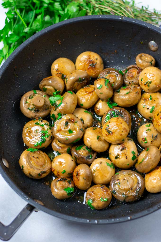 Closeup of the ready Garlic Mushrooms with some fresh herbs in the background.