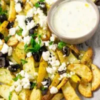 Baking sheet with the ready Greek Fries and a small bowl of homemade Tzatziki sauce for dipping.