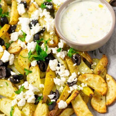 Baking sheet with the ready Greek Fries and a small bowl of homemade Tzatziki sauce for dipping.