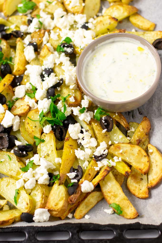 Baking sheet with the ready Greek Fries and a small bowl of homemade Tzatziki sauce for dipping.