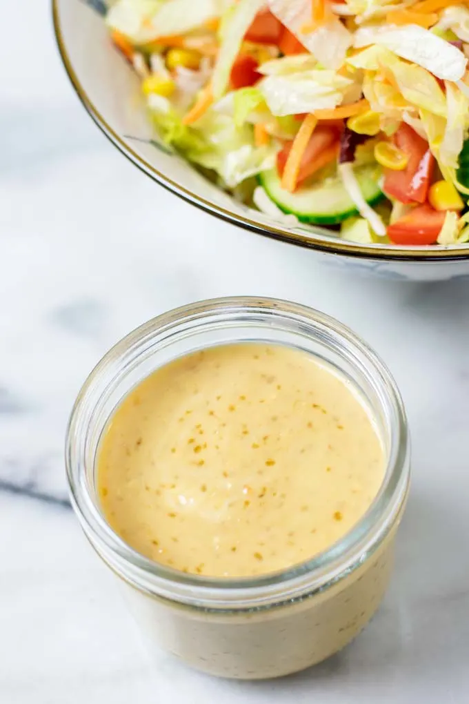 A large bowl of salad with a jar of the Roasted Sesame Dressing in front.