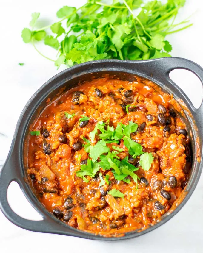 Fresh cilantro is used to garnish the ready chili in a pot.