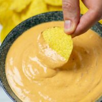 Dipping a tortilla chip into the sauce.