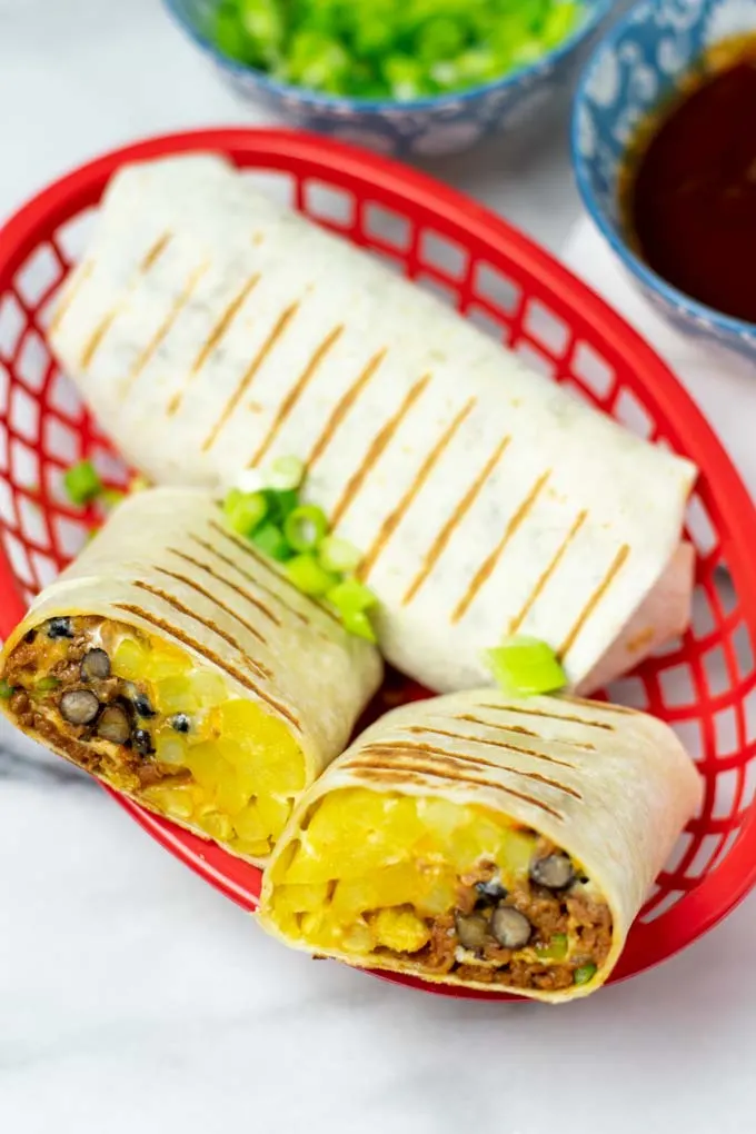 A red basket with one closed and one open cup French Taco revealing the filling.