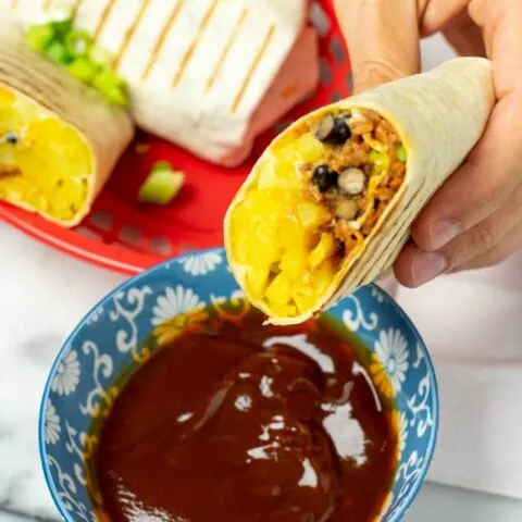A half French Taco is held in one hand over a small bowl with dipping sauce.