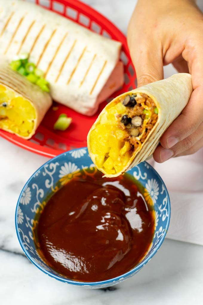 A half French Taco is held in one hand over a small bowl with dipping sauce.