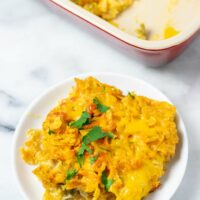 View of a single portion of the Nacho Chicken on a small white plate with the casserole dish in the background.