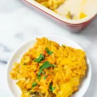 View of a single portion of the Nacho Chicken on a small white plate with the casserole dish in the background.