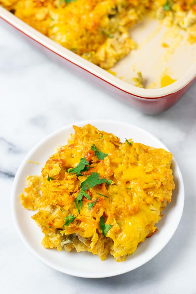 View of a single portion of the Nacho Chicken on a small white plate with the casserole dish in the background.