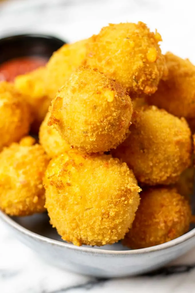 A large stack of ready Potato Cheese Balls on a serving plate, with a small bowl of ketchup in the background.