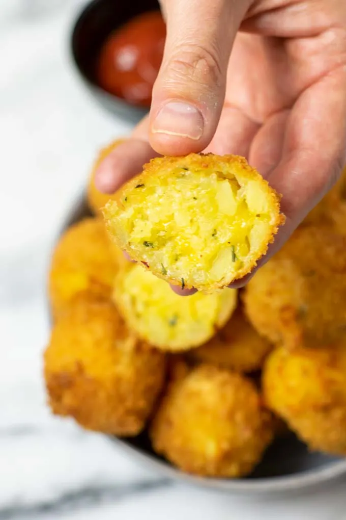 A hand is holding a Potato Cheese Ball sliced open.