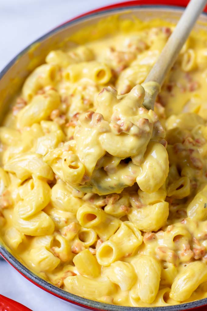 A spoonful of Bacon Mac and Cheese is lifted from a casserole dish.