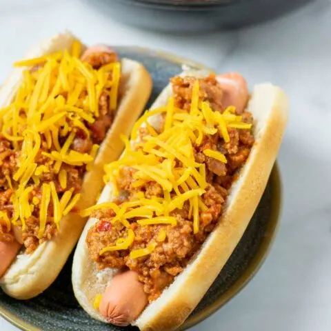 A plate with two hot dogs loaded with the Hot Dog Chili and sprinkled with vegan cheese.